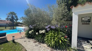 Una zona de piscina con un edificio blanco, rodeada de plantas y flores diversas.