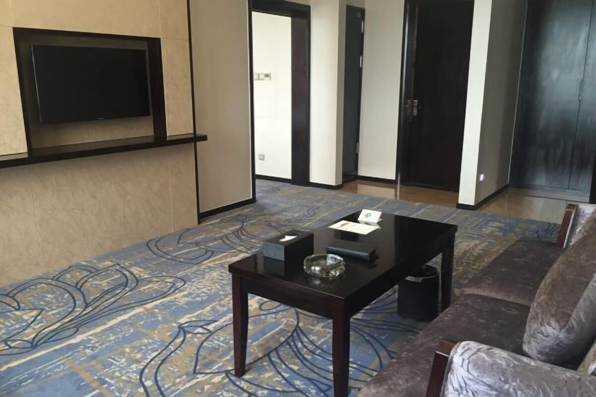 A living room with a sofa, a coffee table, a flat-screen TV mounted on the wall, and a patterned carpet.