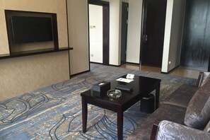 A living room with a sofa, a coffee table, a flat-screen TV mounted on the wall, and a patterned carpet. - Yantai Baohua Mingdu Hotel (Qixia)