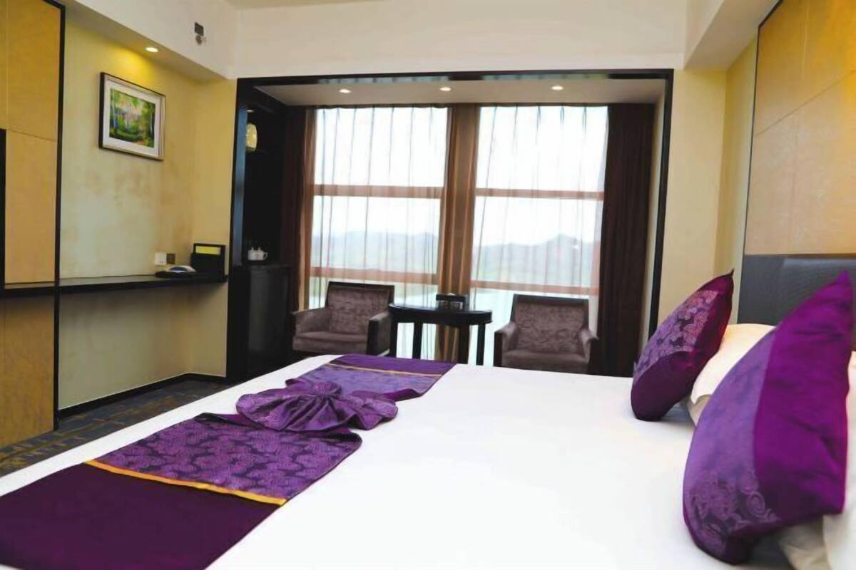 Une chambre d’hôtel avec un lit, deux chaises, une petite table et une vue sur l’extérieur grâce à une grande fenêtre.