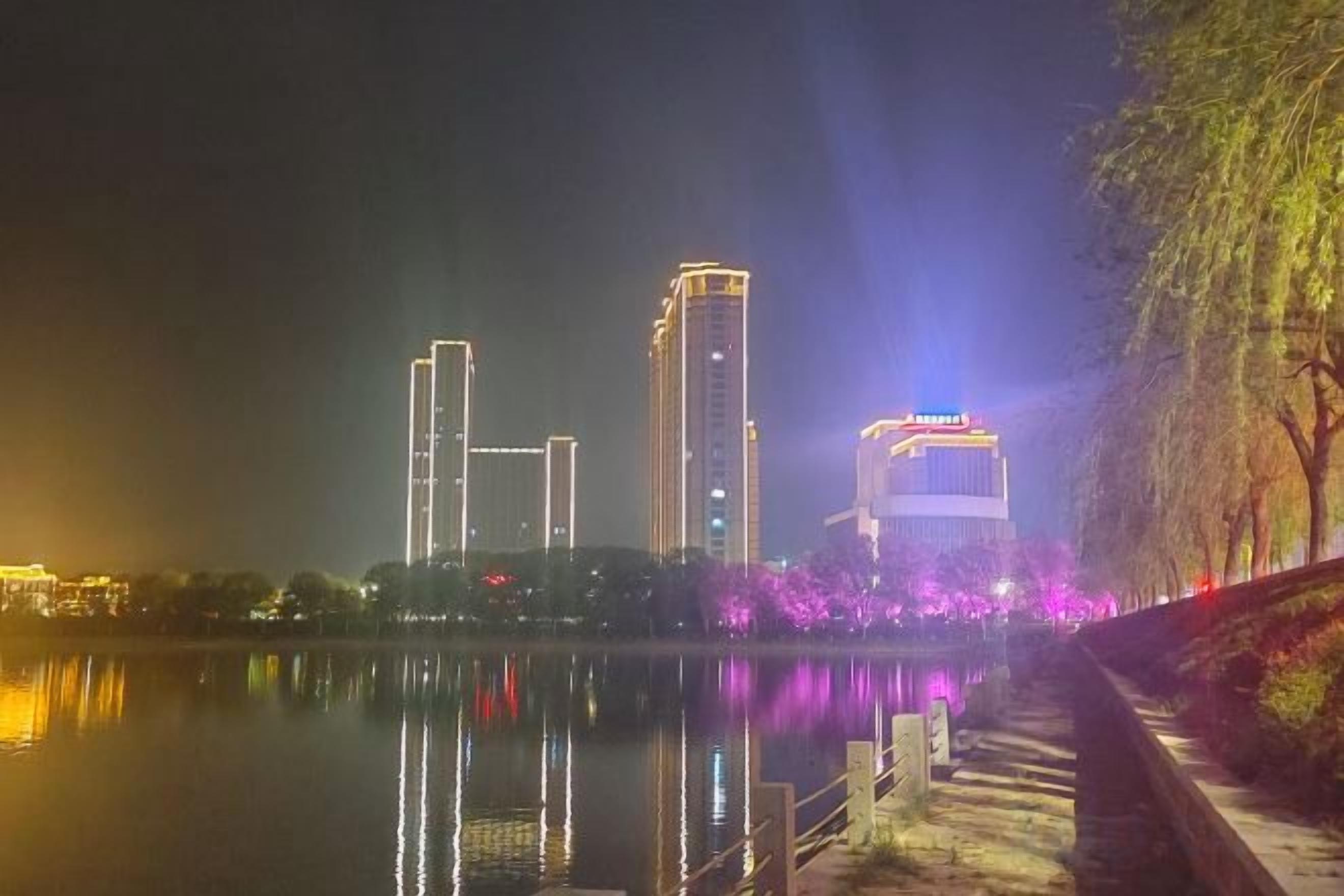 A nighttime cityscape with illuminated buildings and a calm body of water reflecting the lights.