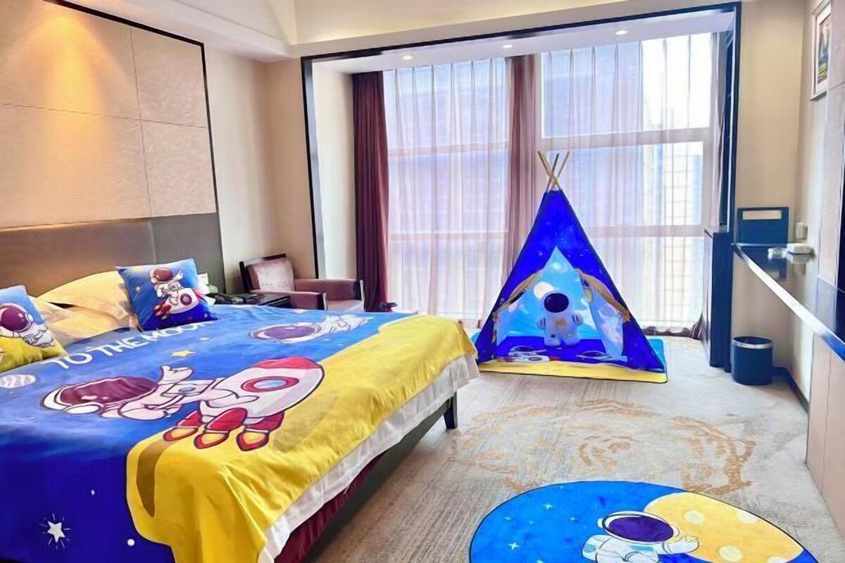 Une chambre d’hôtel avec un lit agrémenté d’une couvre-lit sur le thème de l  ’espace, une fenêtre avec des rideaux légers et une petite structure en forme de tipi ornée d’images d’astronautes.