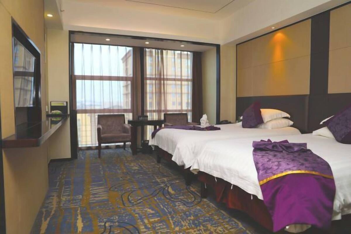Une chambre d’hôtel avec deux lits, un bureau, une chaise et une grande fenêtre.