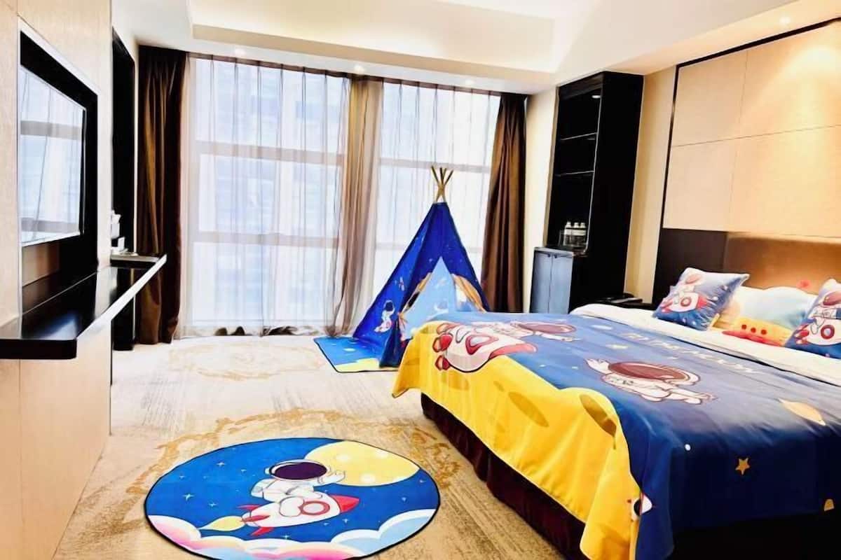Une chambre d’hôtel comprenant un lit, une télévision, une fenêtre avec des rideaux, une petite table et une étagère fixée au mur.