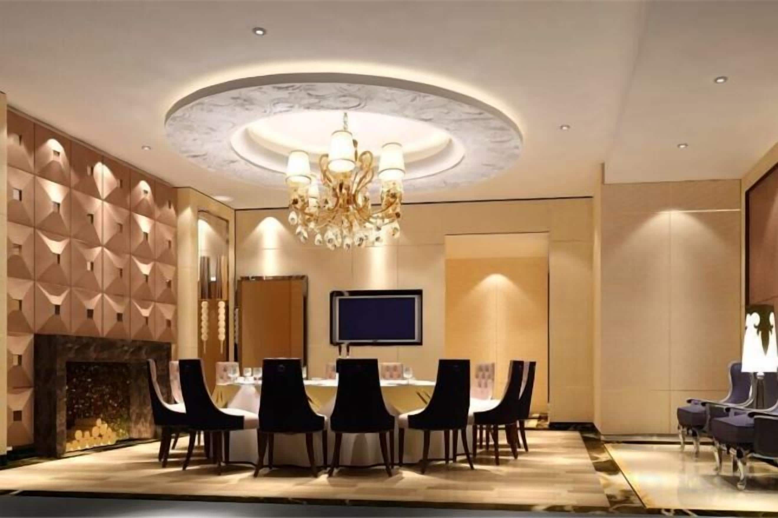 A conference room with a round table, chairs, a chandelier, a flat-screen TV, and a fireplace.
