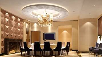 A conference room with a round table, chairs, a chandelier, a flat-screen TV, and a fireplace.