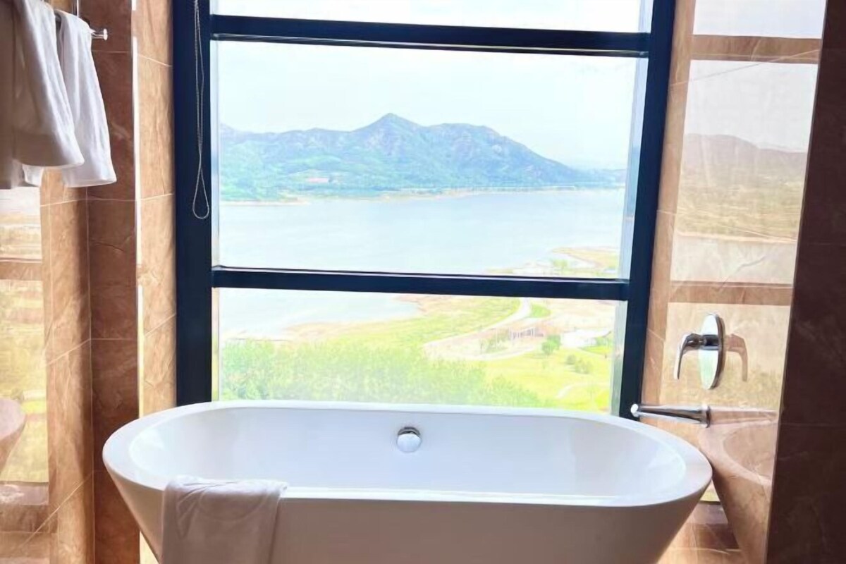 A bathroom with a freestanding bathtub, a window with a view of a lake and mountains, and a towel rack.