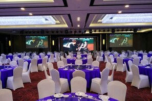 Une salle de banquet avec des tables rondes, des chaises blanches et des nappes violettes.