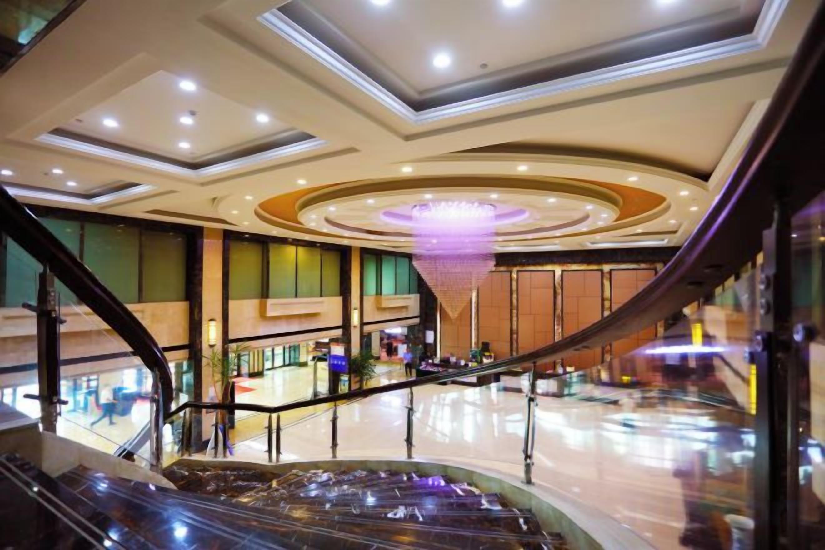An indoor space with a curved staircase, a central chandelier, and a polished floor.