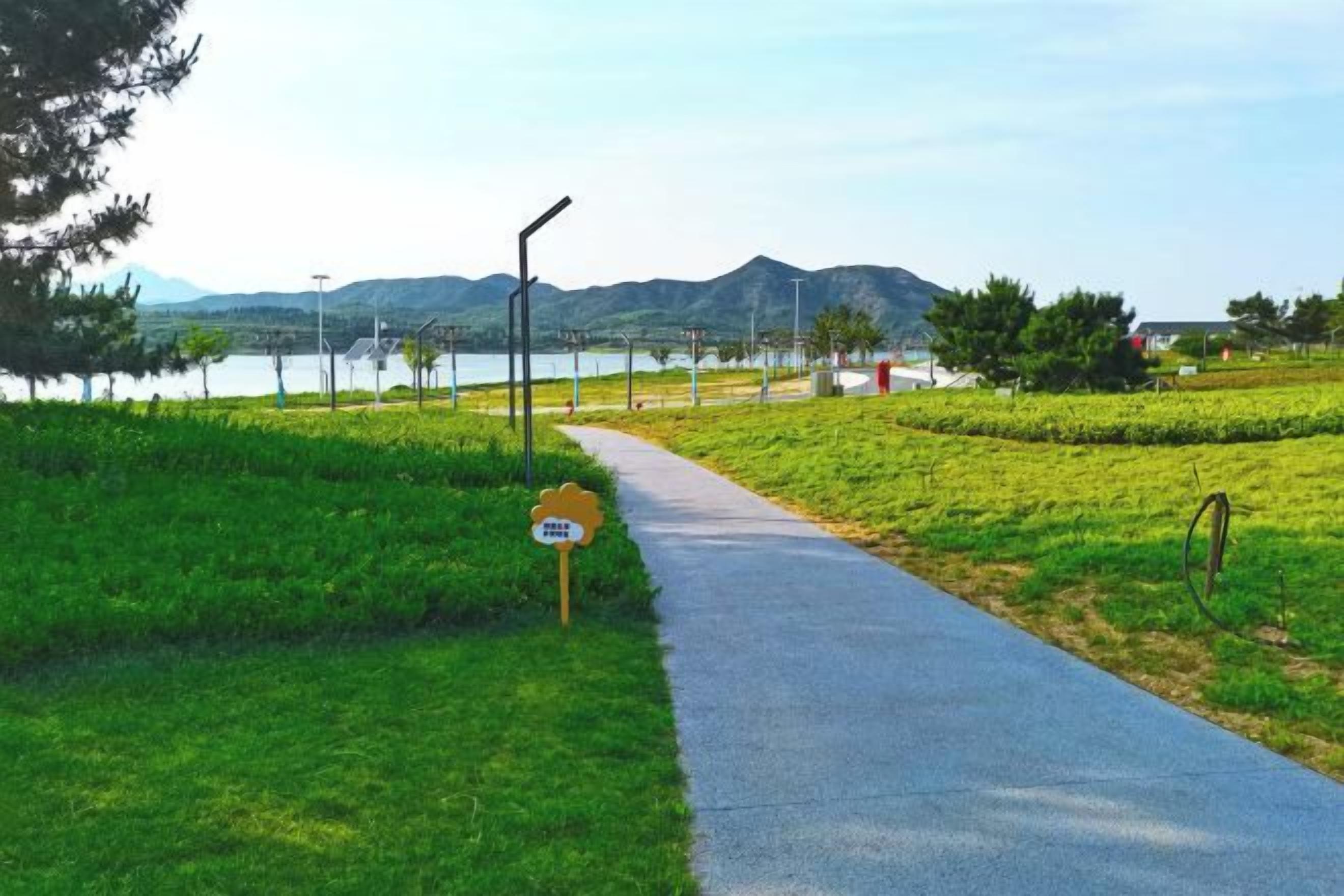A paved pathway alongside a body of water with a mountain backdrop.