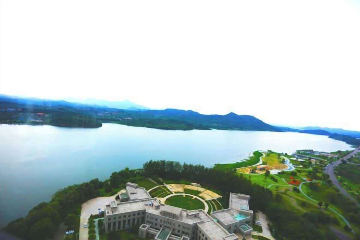 Vue aérienne d’un vaste complexe de bâtiments doté d’une cour centrale circulaire, entouré d’une végétation luxuriante et d’un lac.
