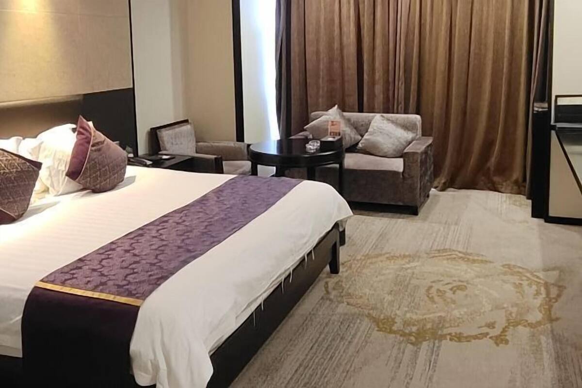 Une chambre d’hôtel avec un grand lit, un canapé, une petite table et une vue sur l’extérieur, visible à travers les rideaux.