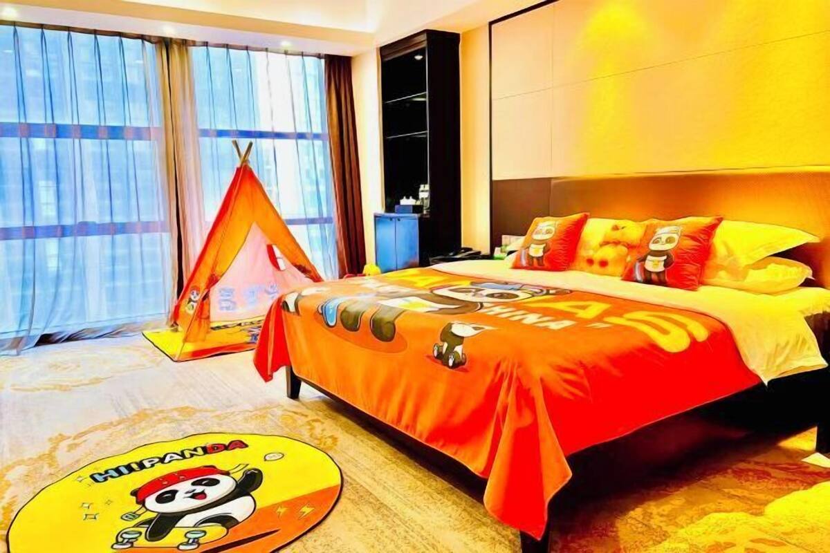 Une chambre d’hôtel avec un grand lit, une fenêtre avec des rideaux, une petite tente et un tapis décoré avec des motifs de pandas.
