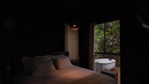 Ein schlafwagenzimmer mit gedämpftem Licht, einem Bett, einem Fenster mit Blick auf Grünflächen und einer Außenwhirlpool.