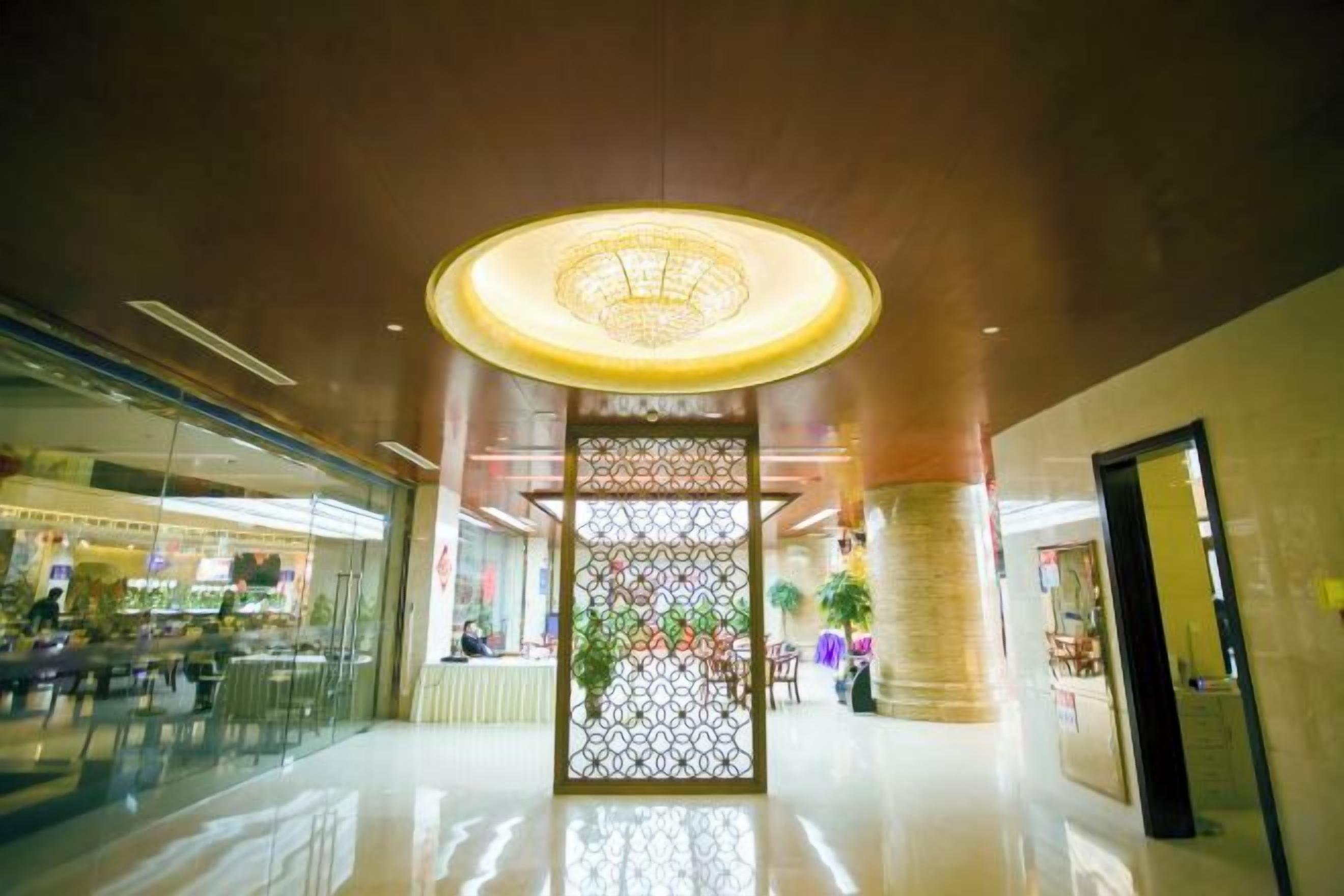 Un lobby amplio con un panel decorativo central, una lámpara circular grande y un escaparate de vidrio a la izquierda.