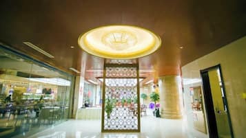 Un lobby amplio con un panel decorativo central, una lámpara circular grande y un escaparate de vidrio a la izquierda.