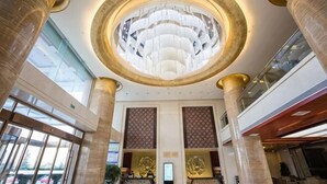 Un vestíbulo con una gran lámpara circular, altas columnas y un mostrador de recepción.