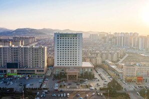 A high-rise building with a central courtyard, surrounded by other buildings, and a parking lot with cars. - Shungeng International Hotel (Jinan)