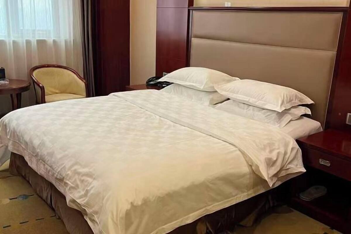 A hotel room with a large bed, a wooden headboard, a bedside table, and a chair.