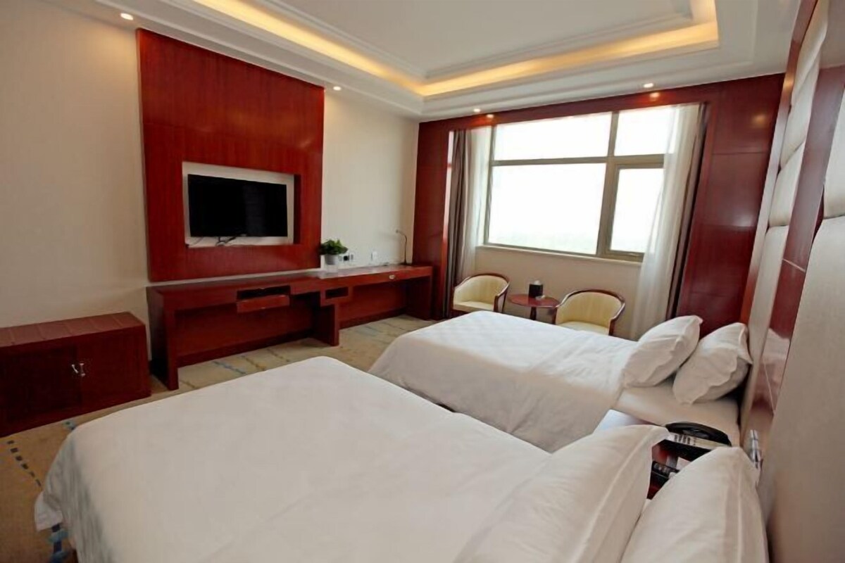 A hotel room with two beds, a TV, a desk, and a window.