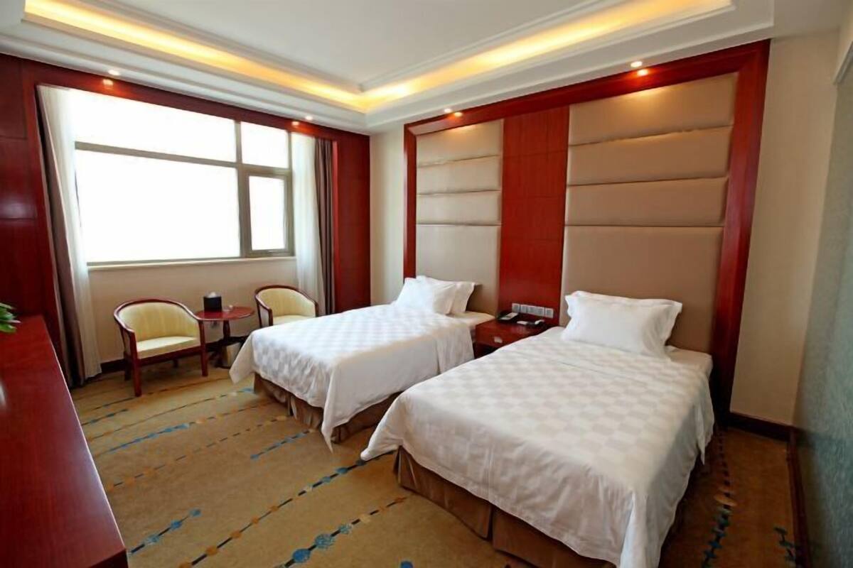 A hotel room with two beds, a desk, a chair, and a large window.