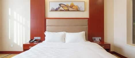 Een hotelkamer met een groot bed, een hoofdbord met een schilderij, twee nachtkastjes en een nachtkastje met een telefoon.