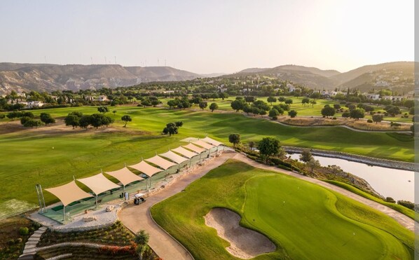 A golf course with a clubhouse, a pond, and surrounding hills.