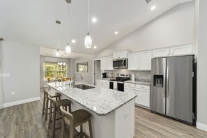 A modern kitchen with white cabinetry, stainless steel appliances, and a granite countertop island with bar stools. - NEW Build--12min WEC Horses, 17min FAST, 42min Silver Springs State Park. 4beds. (Ocala)