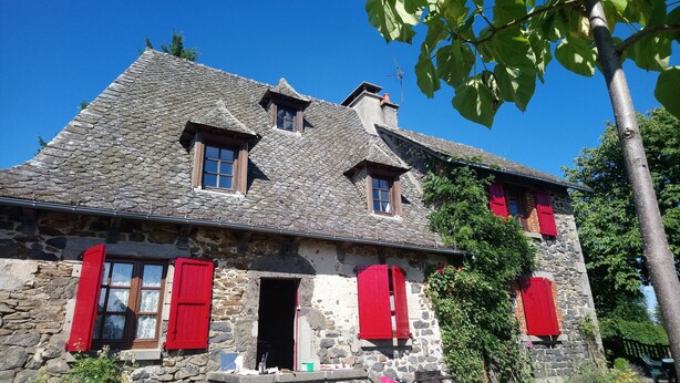 A stone building with red shutters, a chimney, and a clear blue sky.