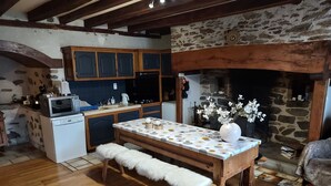 A rustic kitchen with wooden cabinets, a stone wall, and a fireplace.
