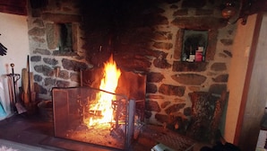 A stone fireplace with a visible fire, a wooden bench, and a stack of newspapers.
