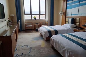 Een hotelkamer met twee bedden, een bureau, een stoel, een televisie en een raam met uitzicht.