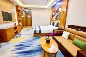 Habitación de hotel con cama, sofá, televisión y una pequeña mesa con una planta.