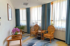 Une chambre d’hôtel avec une grande fenêtre, deux chaises en bois, une petite table et une plante en pot.
