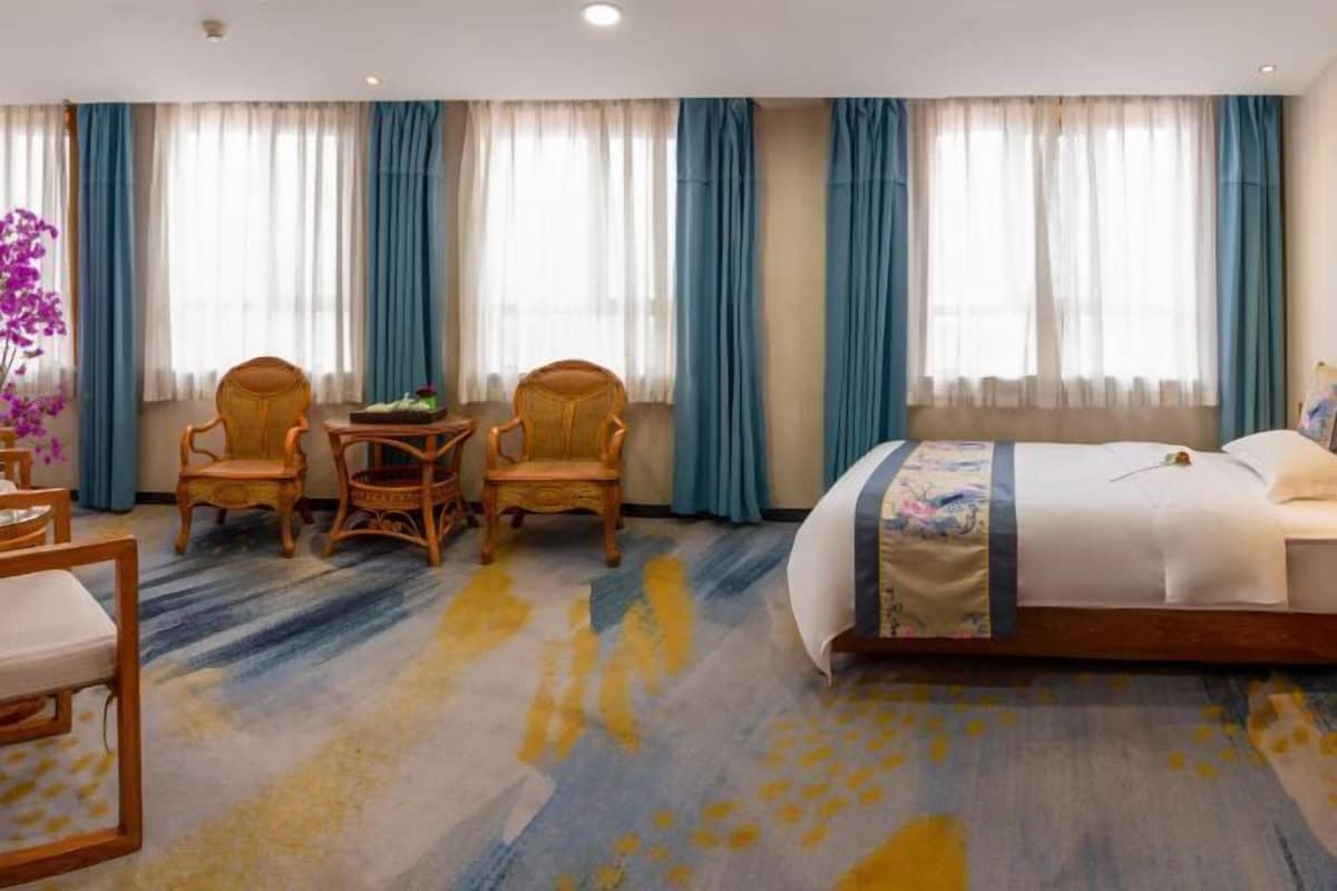 Ein Hotelzimmer mit einem Bett, zwei Stühlen, einem kleinen Tisch und einer Blumenvase.