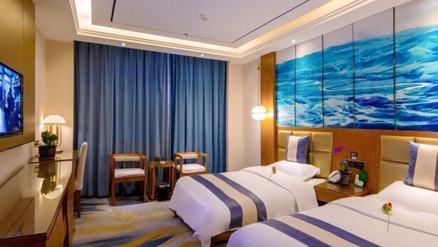 Une chambre d’hôtel avec deux lits, un bureau, une chaise, une télévision et un grand tableau abstrait accroché au mur.