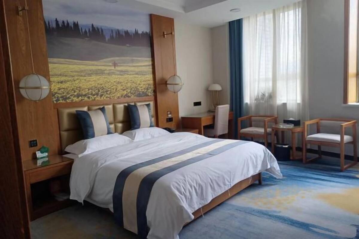 Habitación de hotel con una cama grande, un escritorio, dos sillas, una lámpara y un cuadro en la pared.