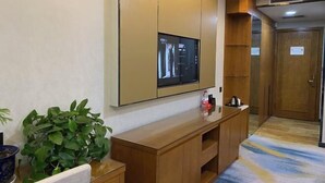 Une chambre d’hôtel dotée d’un grand téléviseur à écran plat fixé au mur, d’une console en bois, d’une plante en pot et d’une porte avec une pancarte.