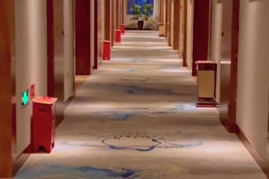 Een hotelgang met een tapijtvloer, deuren aan beide kanten en een prullenbak in het midden.