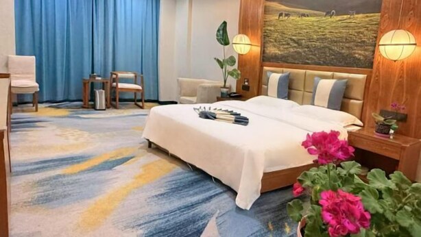 Ein Hotelzimmer mit Bett, Schreibtisch, Stuhl, einer Topfpflanze und einem Bild an der Wand.