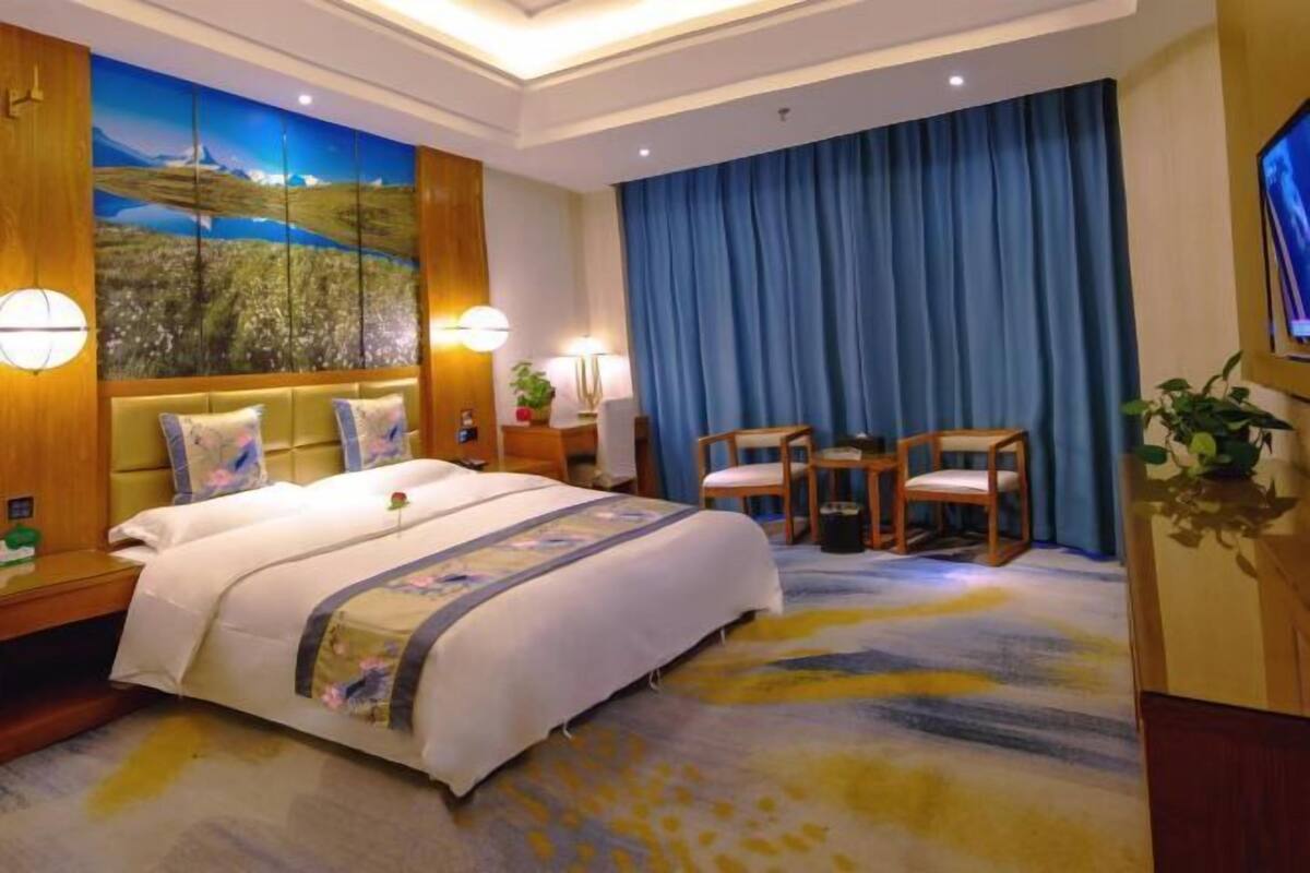 Habitación de hotel con cama, escritorio, dos sillas, televisor y un cuadro grande en la pared.