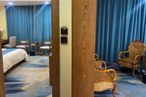 Ein Hotelzimmer mit einem Bett, zwei Stühlen, einem kleinen Tisch, einem Holzschrank und einem blauen Vorhang.