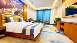 Ein Hotelzimmer mit einem großen Bett, einem an der Wand montierten Fernseher, einem Schreibtisch mit Stuhl und einem blauen Vorhang.