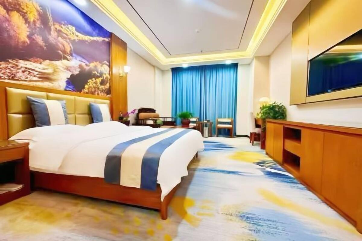 Una habitación de hotel con una cama grande, un televisor montado en la pared, un escritorio con una silla y una cortina azul.