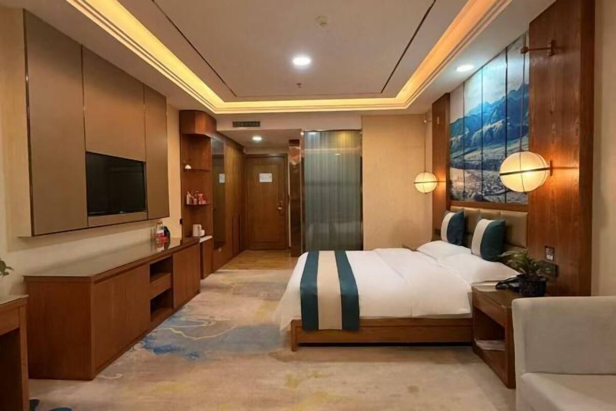 Una habitación de hotel con cama, televisión, muebles de madera y un cuadro en la pared.