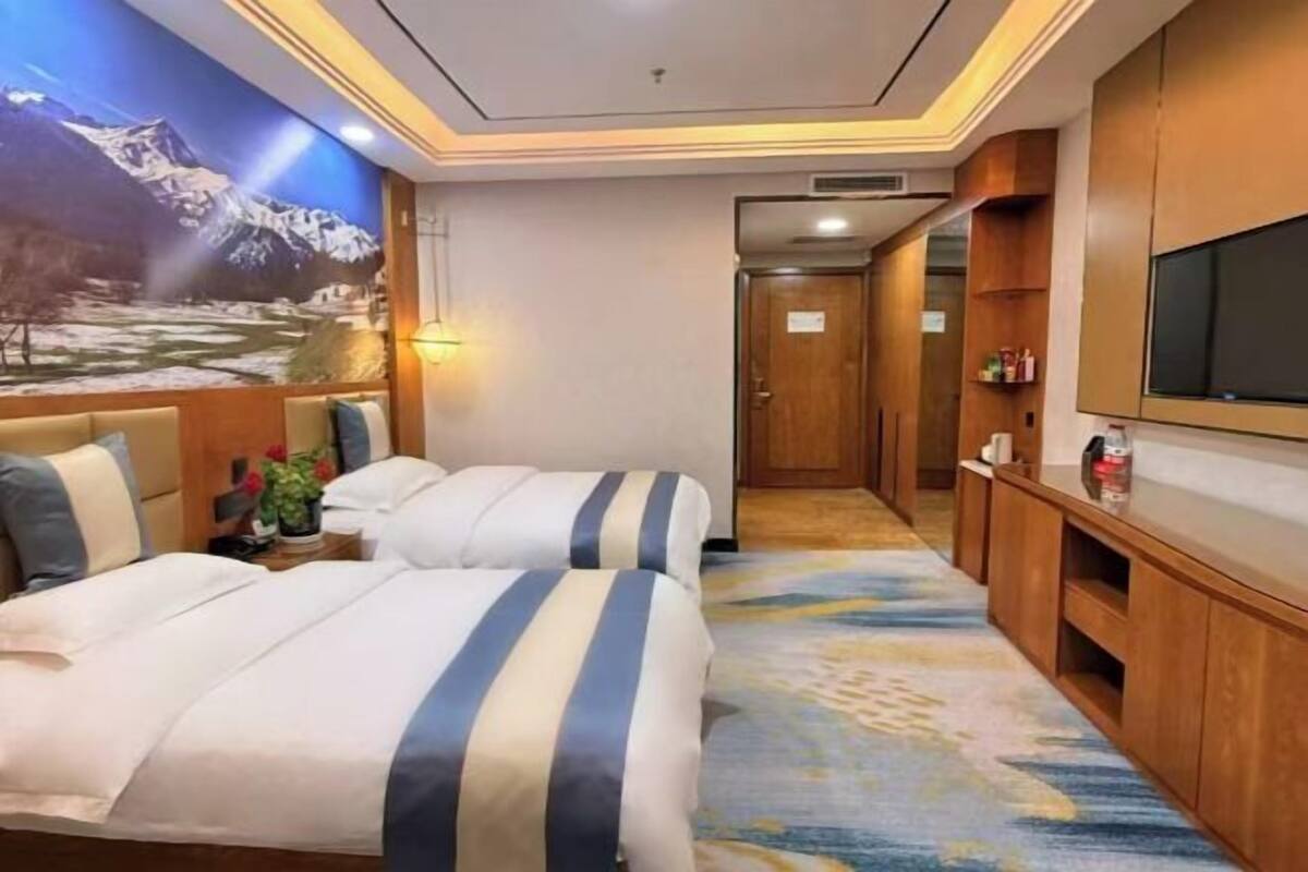 Una habitación de hotel con cama, televisor, aparador de madera y un mural en la pared.