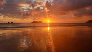 A beach at sunset with the sun low on the horizon, reflecting on the wet sand.