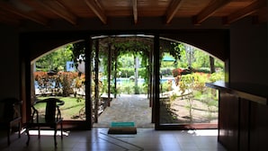 An arched doorway leading to a garden with a stone pathway, wooden ceiling, and a bench inside.