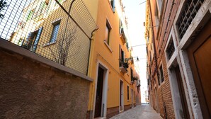 A narrow cobblestone street flanked by yellow buildings with balconies and a mesh fence. - Biennial-Pulse (Venezia)