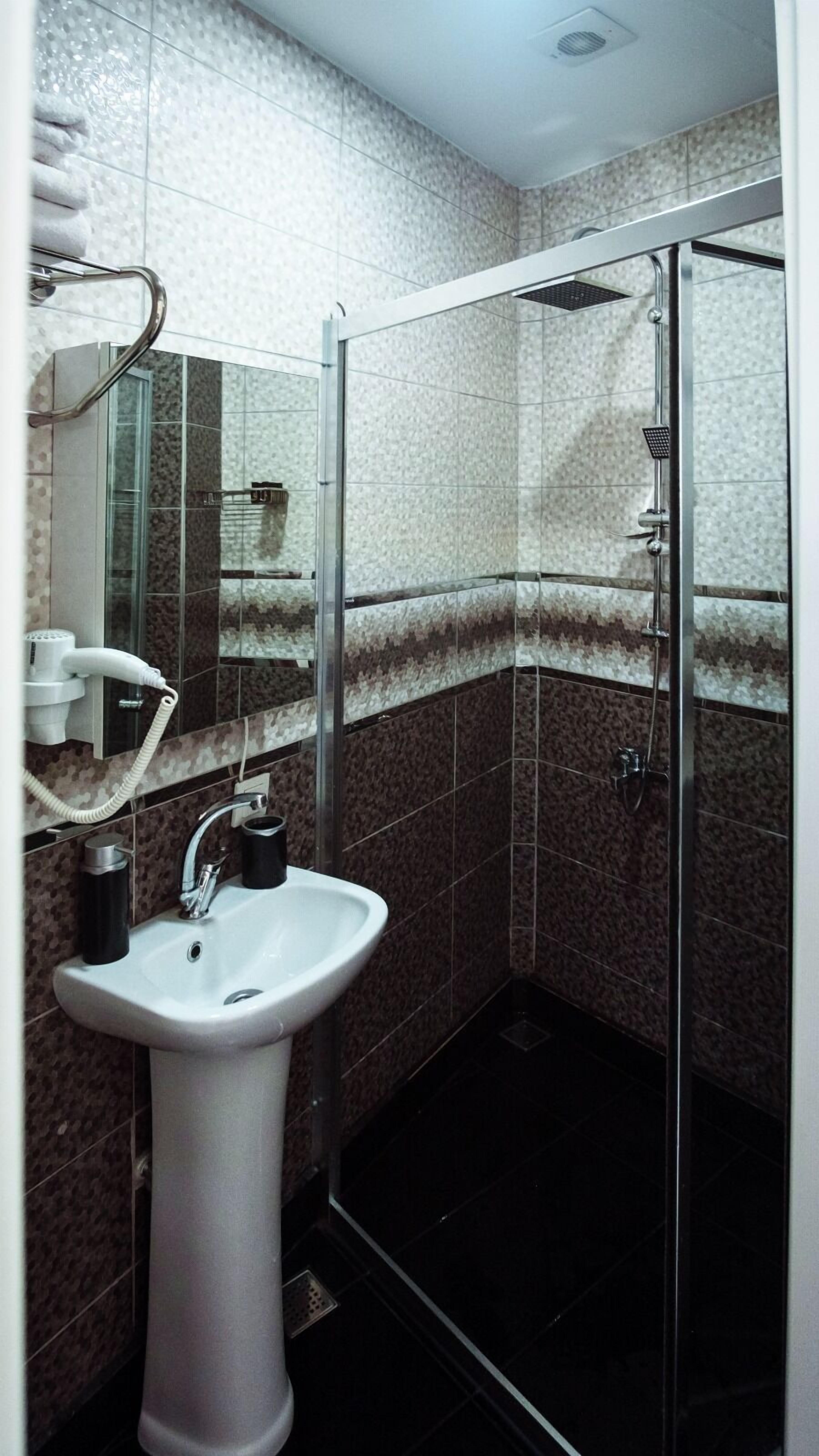 A bathroom with a white pedestal sink, a glass shower enclosure, and a mirror above the sink.